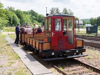 Das Bild zeigt eine Lok der Chemnitztalbahn auf Gleisen. In einem angehängten Waggon sitzen Menschen.