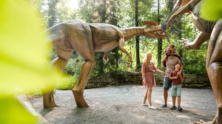 Ein Familie bestehend aus einem Mann, einer Frau und zwei kleinen Kindern stehen im Sauerierpark Kleinwelka. Links und Rechts von ihnen befinden sich Dinosaurierfiguren.